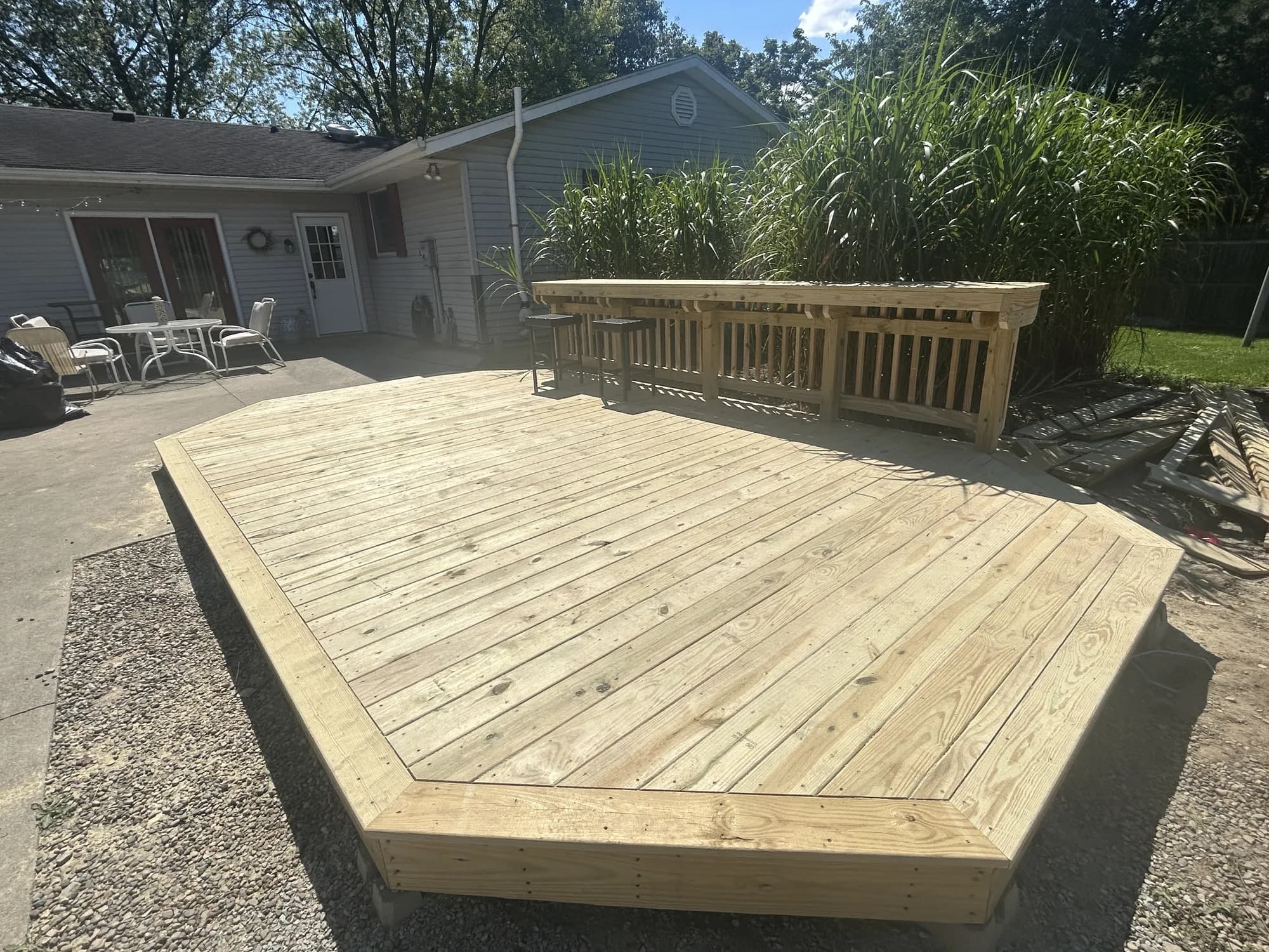 Ground-level pressure-treated backyard deck with angled corners and a built-in bar counter with stools