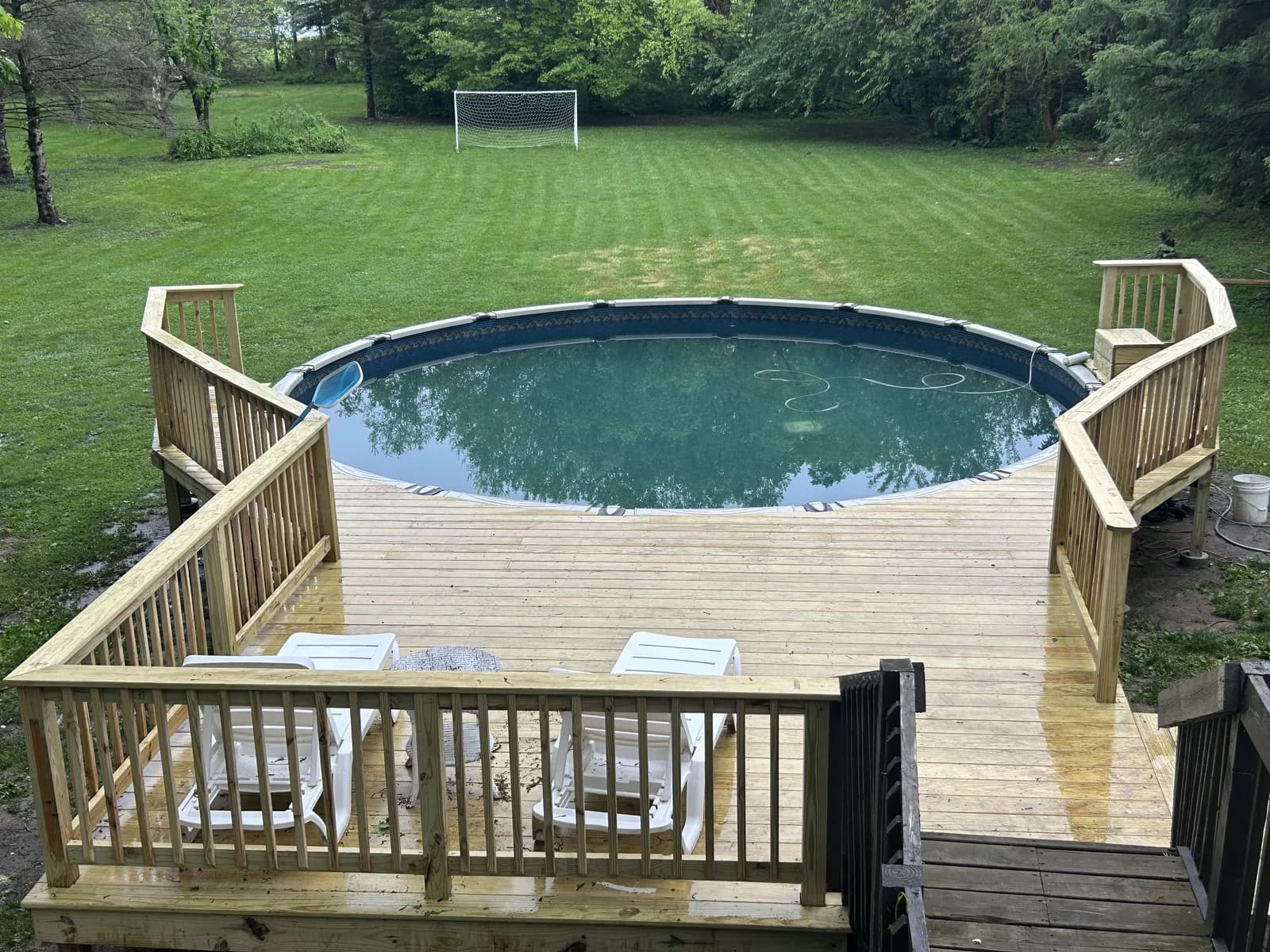 Pressure-treated pool deck with wide stairs and railings around an above-ground pool