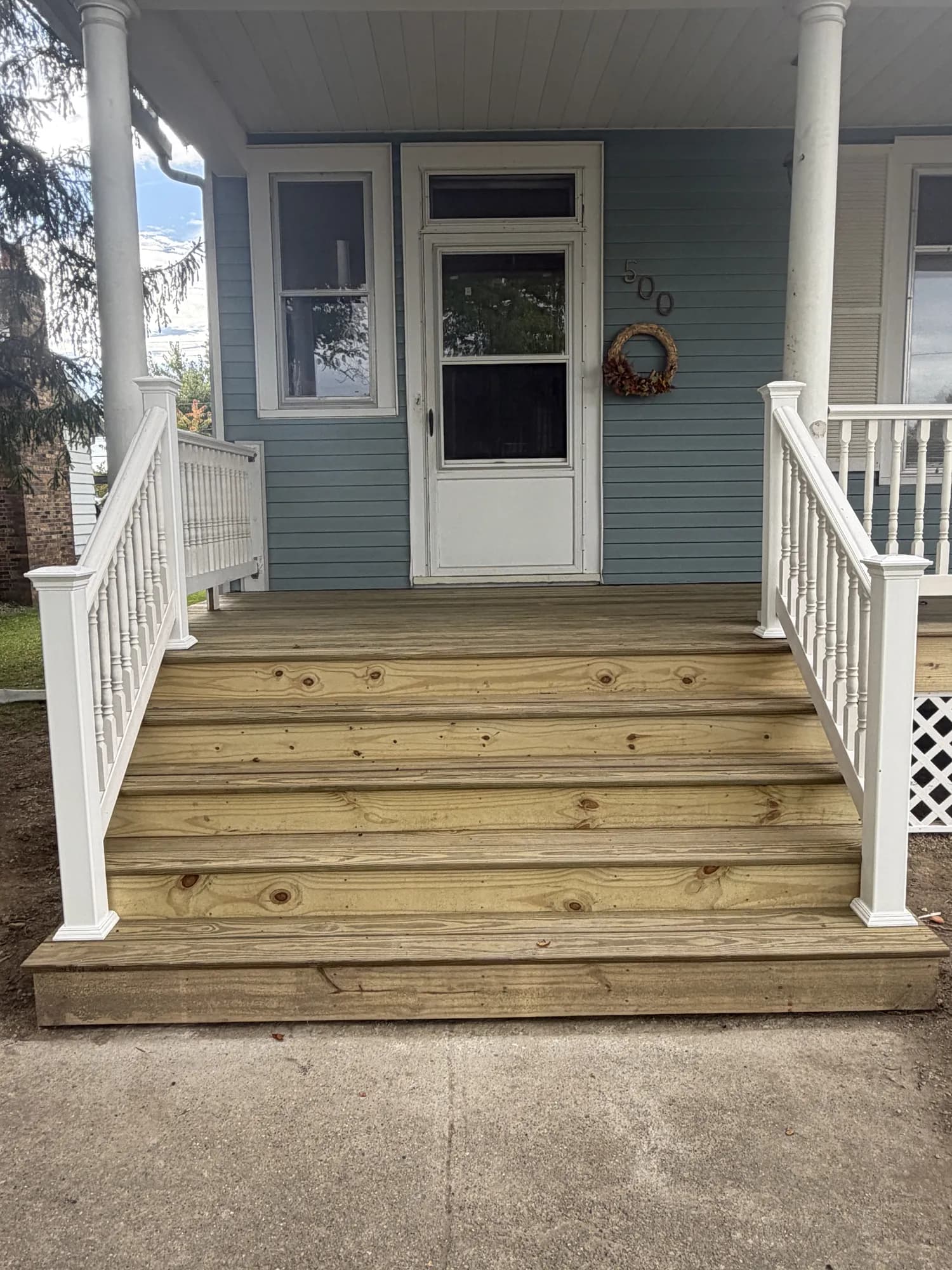 New pressure-treated front porch steps with white spindle railings leading to a blue house