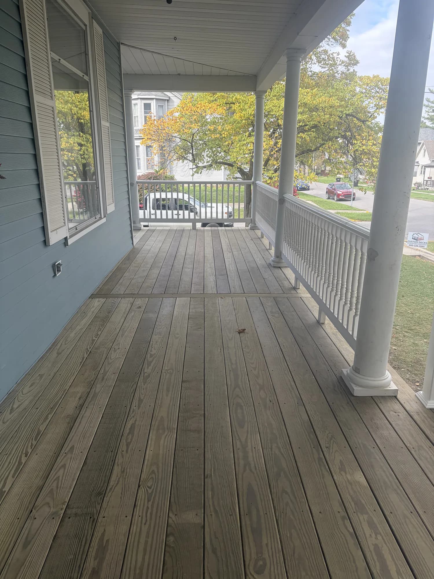 New pressure-treated decking wrapping around the corner of a covered front porch with white columns
