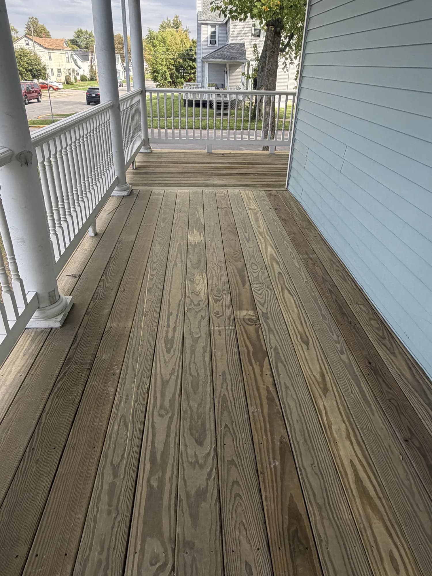 Long run of new pressure-treated porch decking along the side of a house with white railings