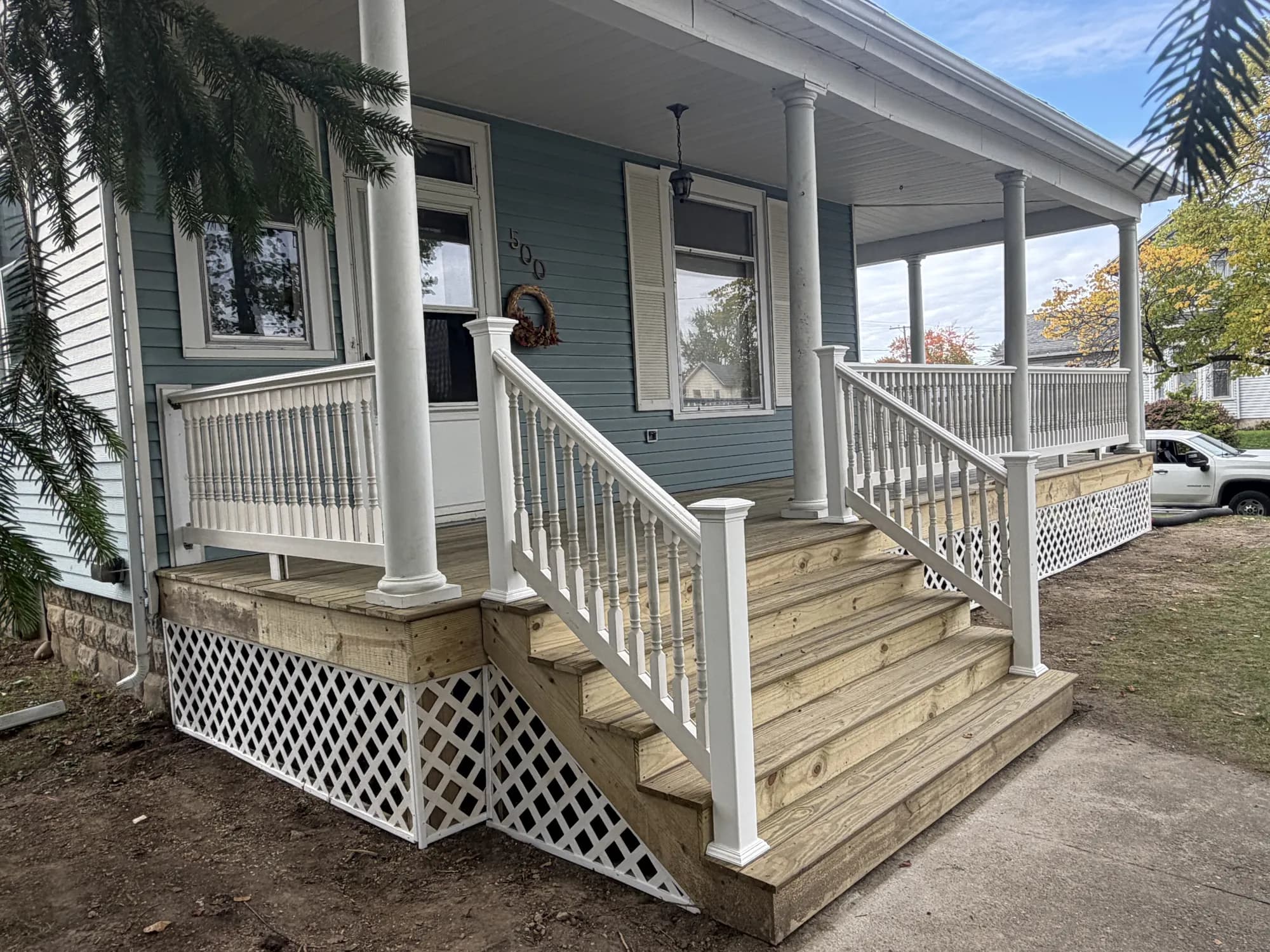 Rebuilt wraparound front porch with new pressure-treated decking, wide steps, white railings and lattice skirting